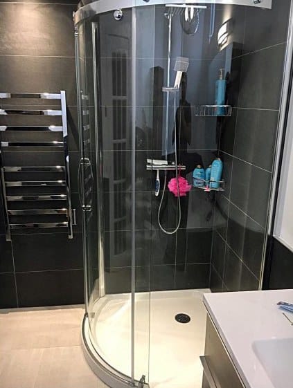 A modern bathroom with a curved glass shower in the corner, black tiled walls, and a silver towel rack