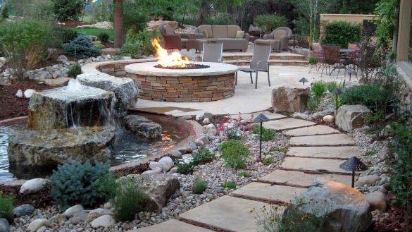 Backyard with stone path, fire pit, waterfall, and outdoor seating surrounded by greenery