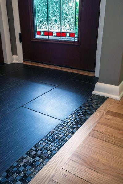 Elegant tile-to-wood floor transition in a foyer, featuring sleek black tiles with a mosaic border blending into natural wood
