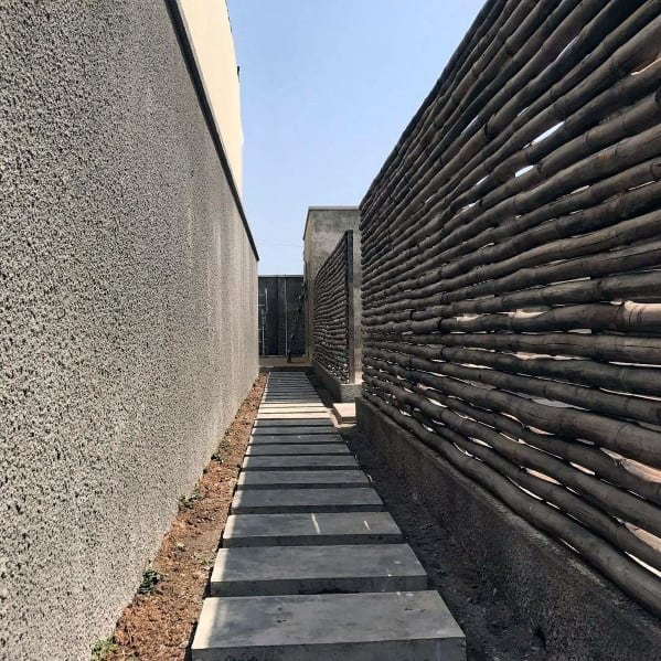 Horizontal bamboo fence along a narrow concrete walkway with large stepping stones.
