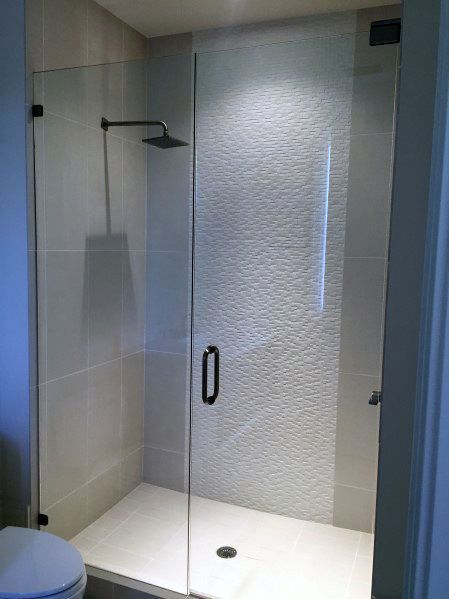 Glass-enclosed shower with textured white walls and sleek black fixtures on the floor