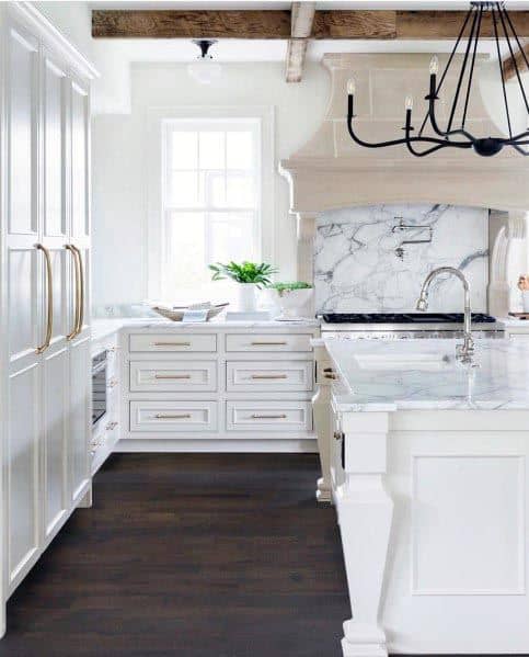 White kitchen with marble countertops, exposed beams, and a black chandelier.