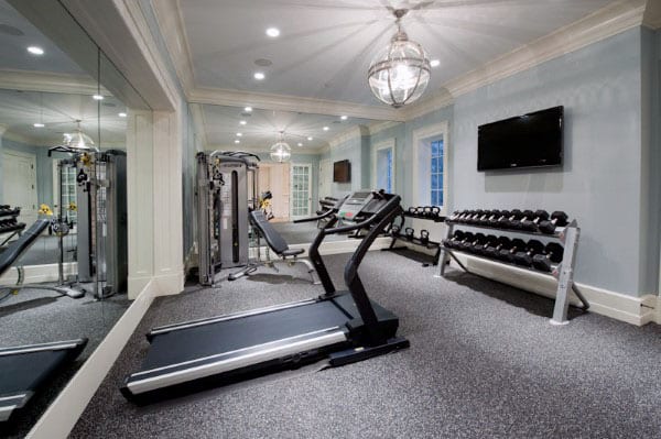Home gym with treadmill, weight rack, exercise machines, and home TV on a light blue wall