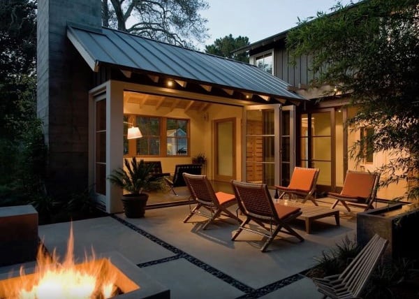 Cozy patio with red chairs, a fire pit, and warm lighting surrounded by trees