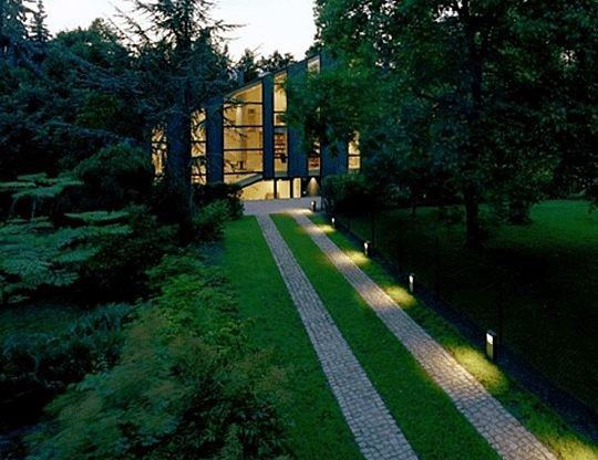 Modern driveway lined with sleek post lighting, casting a soft glow along the cobblestone path leading to a contemporary home