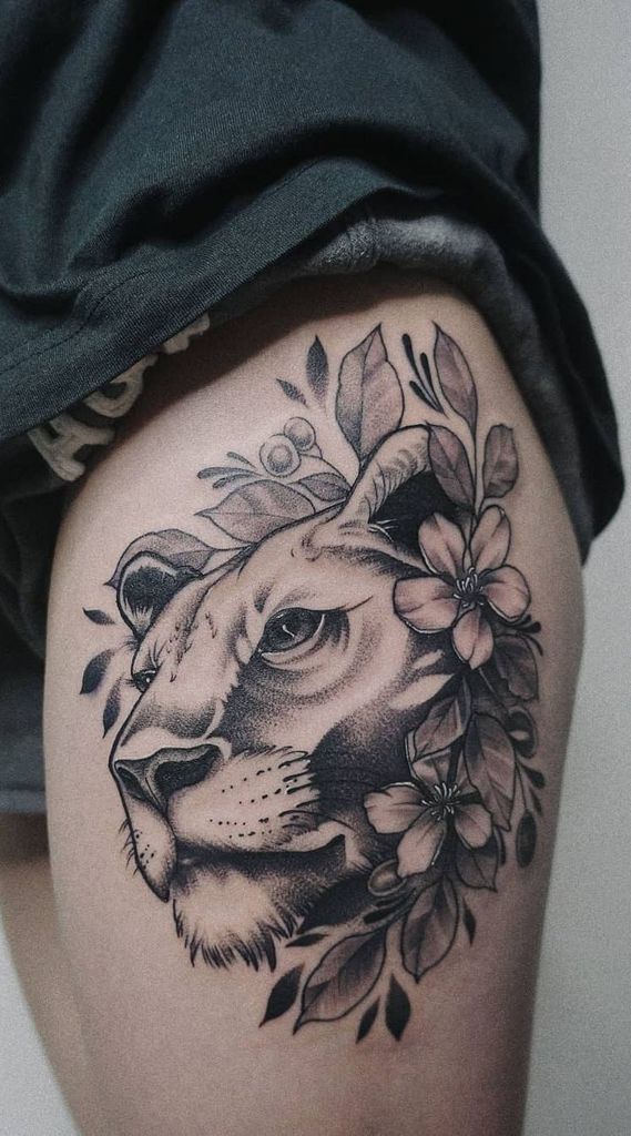 Black and grey lioness thigh tattoo with bold shading, floral details, and fine linework, creating a powerful yet elegant design.
