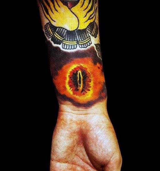 Forearm tattoo featuring the Eye of Sauron, encircled by intricate, fiery designs on a black background