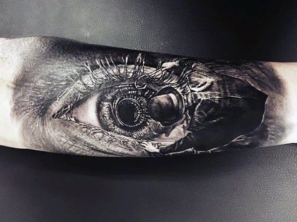 Forearm tattoo of a detailed human eye with a mechanical component in the iris