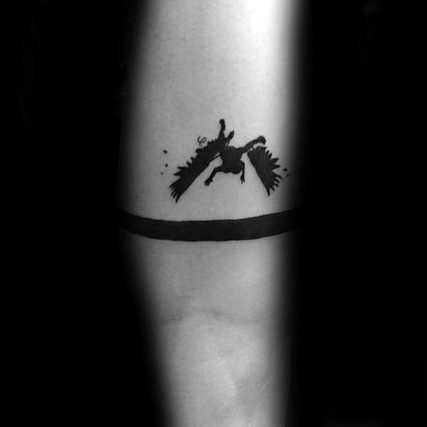 Silhouette tattoo of a falling winged figure above a solid black armband, inked on the inner forearm.