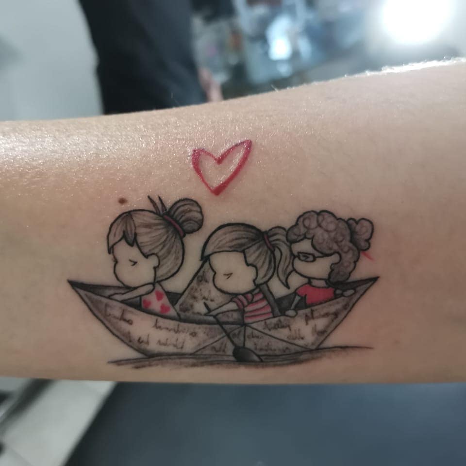 Tattoo of three cartoon girls characters in a paper boat with a red heart above them, depicting friendship or family