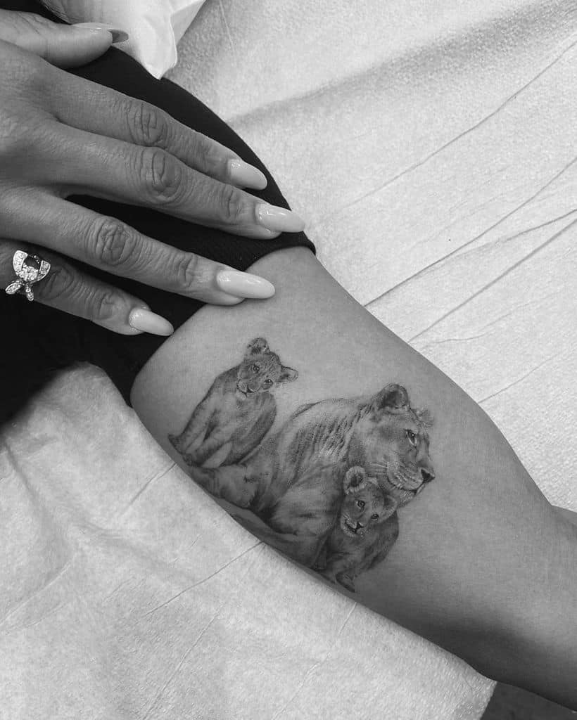 Realistic lioness and cubs tattoo on the thigh, featuring fine shading and intricate details to capture the bond of a mother and her young.