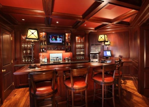 A cozy home bar with wooden décor, red ceiling, bar counter, and a TV screen above the bottles