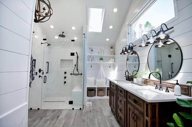Modern bathroom with a glass shower, farmhouse wooden cabinets, dual sinks, round mirrors, and overhead lighting