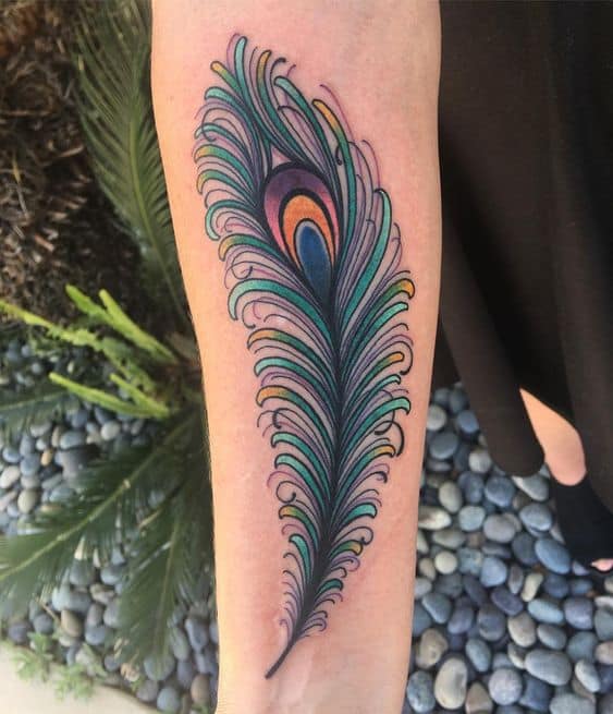 Colorful peacock feather tattoo on the forearm, featuring intricate detailing, vibrant green, blue, and orange hues, and fine linework.