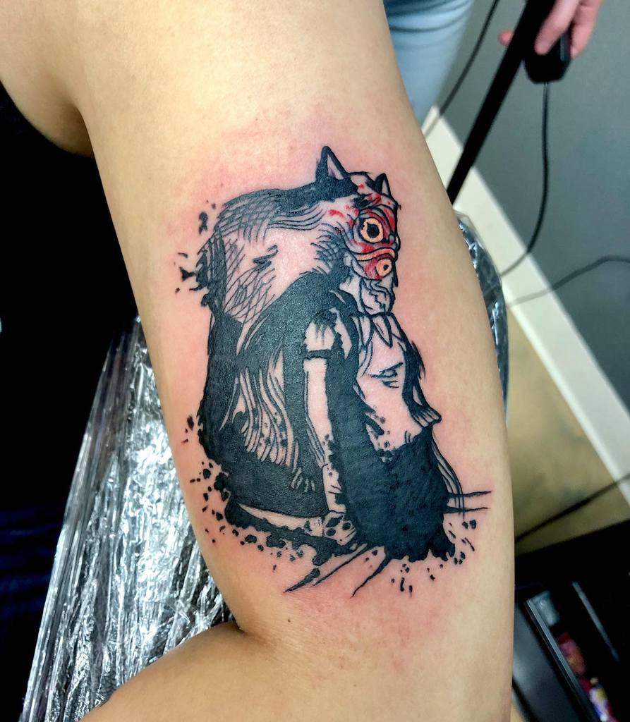 A dynamic tattoo design featuring a character with a mask, surrounded by bold ink splashes and strokes. The tattoo showcases the character's detailed features and dramatic shading.