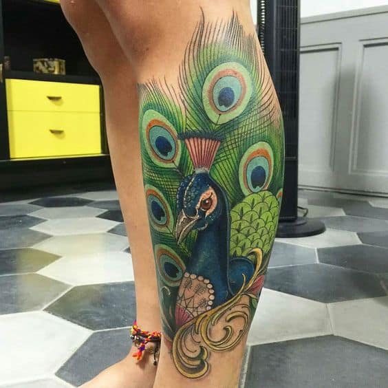 Vibrant peacock tattoo on the leg, featuring intricate feather details, rich blue and green hues, and ornate decorative elements for a bold design.