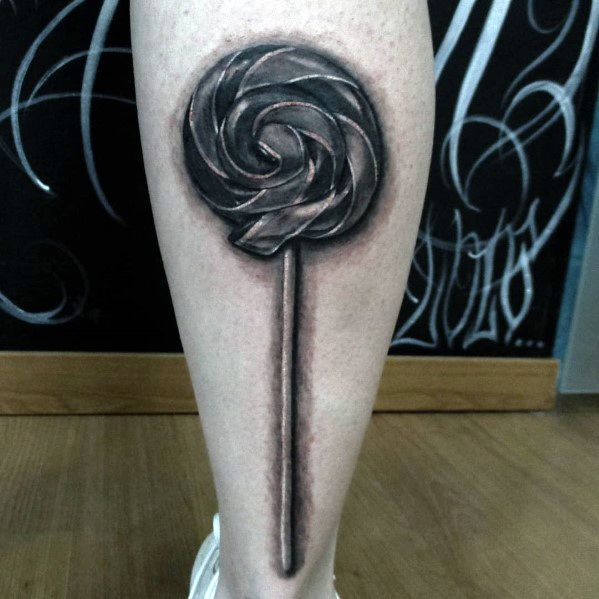 Realistic black and grey lollipop tattoo with detailed shading, creating a striking 3D effect on the leg.