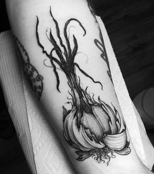 Detailed black and grey garlic tattoo with long roots and peeled cloves, featuring fine linework and shading for a bold botanical design.