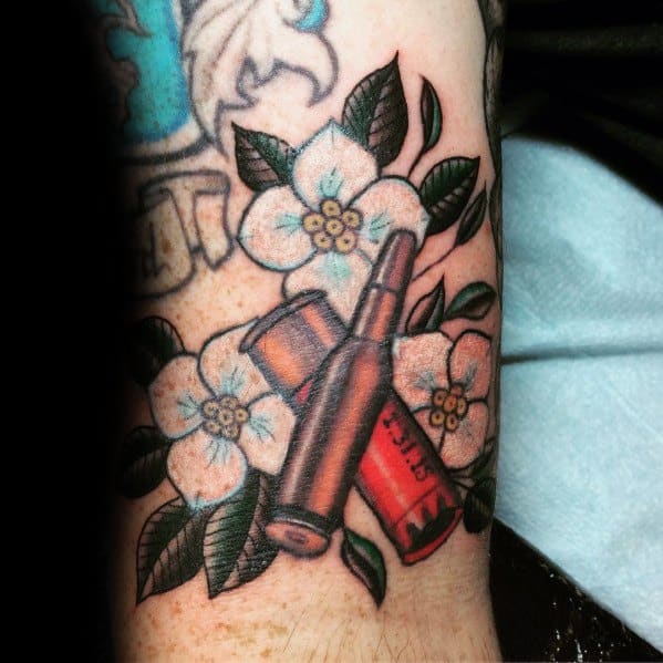 Shotgun shell and rifle bullet tattoo surrounded by white flowers and green leaves, blending bold firepower with delicate nature elements.