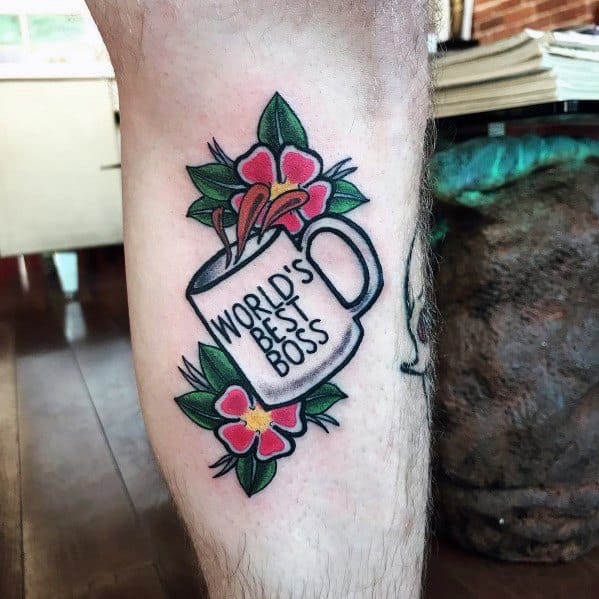 Color tattoo of Michael Scott’s "World’s Best Boss" mug from The Office, surrounded by flowers, adding a decorative touch to the iconic reference.