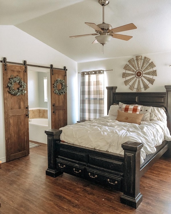 Rustic wood double barn doors in farmhouse-style bedroom with dark wood bed and windmill decor.