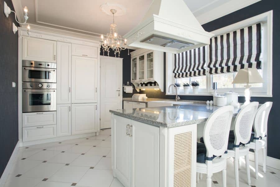 Elegant kitchen with white cabinets, black walls, striped window shades, and chandelier lighting.