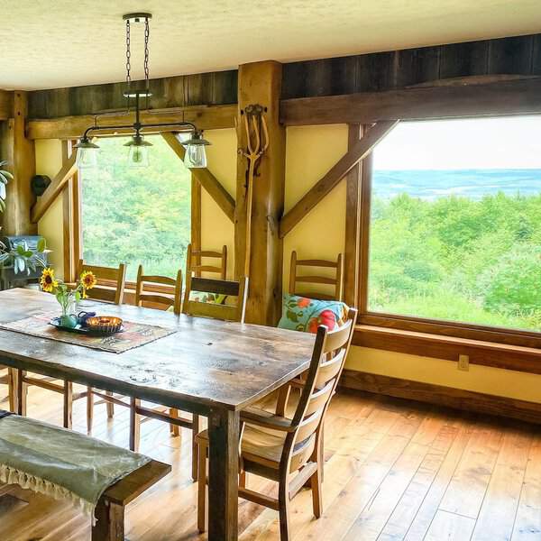 Boho dining room with farmhouse style, rustic wooden table, and large windows offering scenic views.