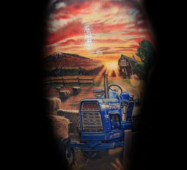 Vibrant tattoo of a blue tractor in a hayfield at sunset, with a barn, fence, and glowing sky in the background.
