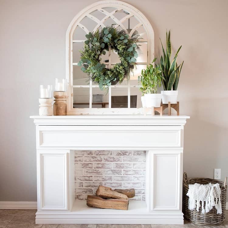 faux white fireplace with candles and pot plants on mantel