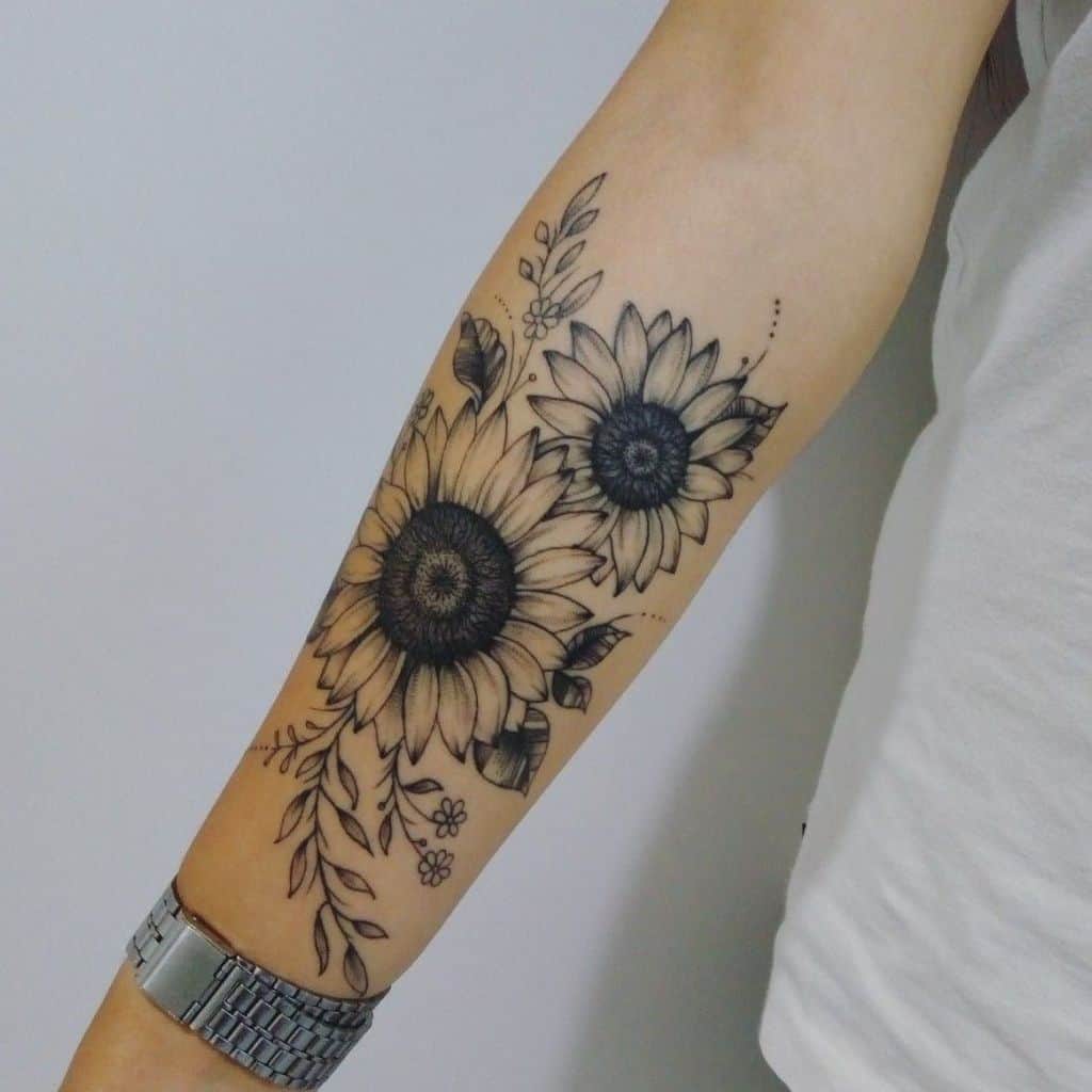 Black and grey sunflower tattoo on forearm featuring two bold blooms, delicate leaves, and fine line floral details for an elegant design.