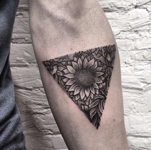 Black and grey sunflower tattoo on upper arm with a triangular design, featuring intricate shading and fine line floral details.