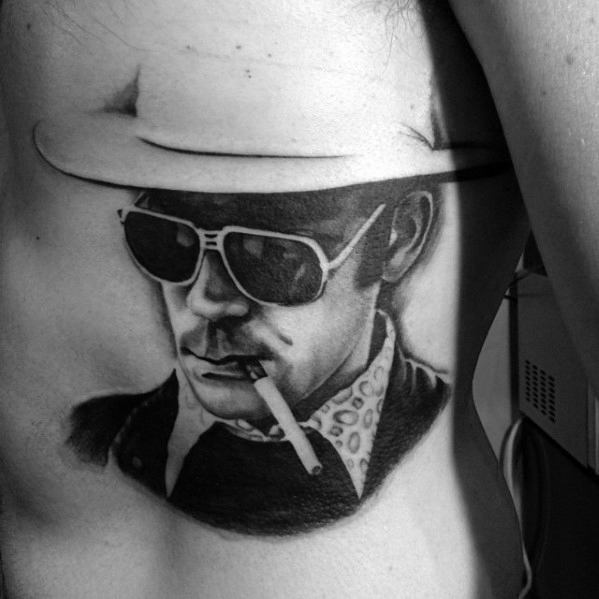 Black and white Hunter S. Thompson tattoo featuring his iconic hat, dark sunglasses, and a cigarette, with bold shading and sharp details.