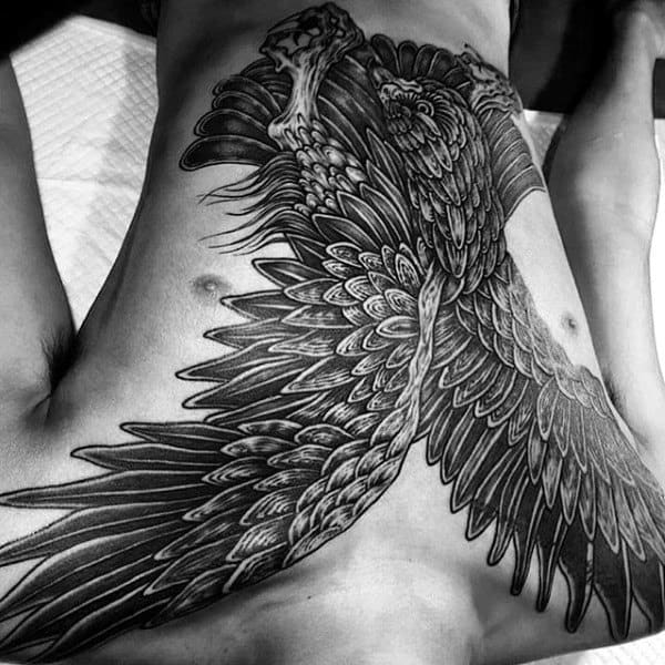 A detailed black and white tattoo of a bird with spread wings on a person's back