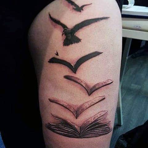 Tattoo of a book turning into birds flying upward on a person's upper arm