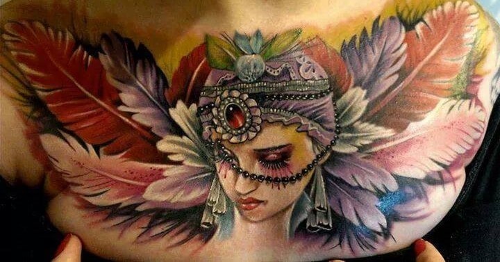 Vibrant chest tattoo of a gypsy woman with an ornate jeweled headpiece, beaded details, and colorful feathers surrounding her.