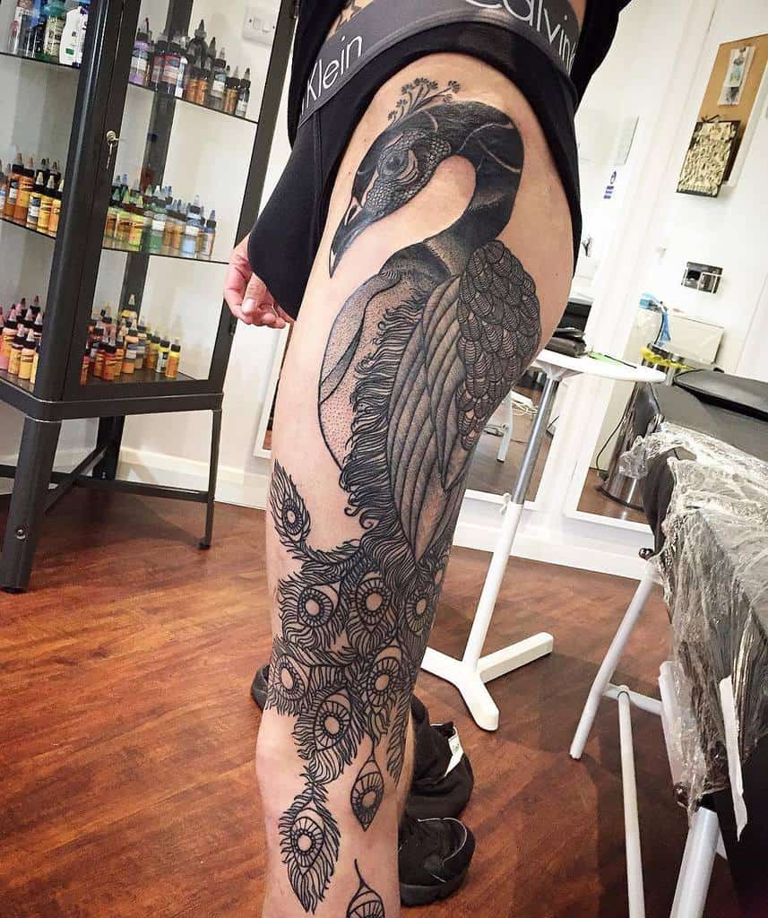 Black and white peacock tattoo covering the thigh with detailed feather patterns and intricate peacock eyes.