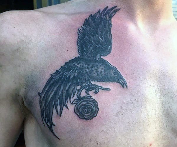 Tattoo of a raven with outstretched wings perched on a rose on a person's upper chest