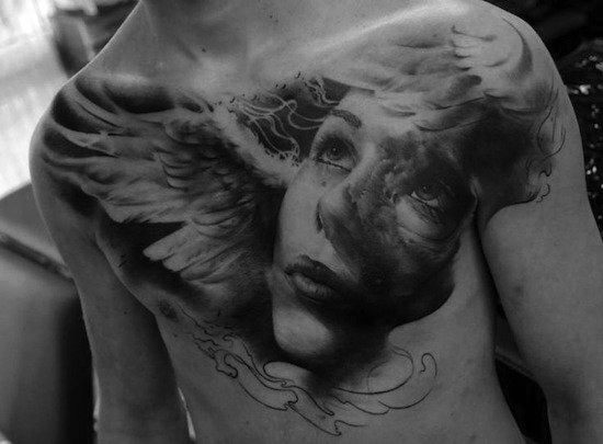 Black and white tattoo of an angelic face with wings on a person's chest