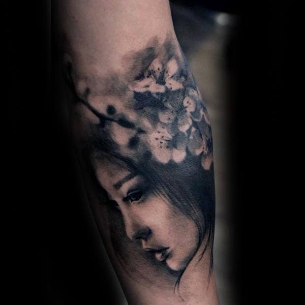 Realistic forearm tattoo featuring a delicate female portrait with soft shading, blended with cherry blossom branches and flowers