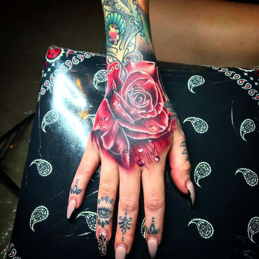 Hand tattooed with an intricate rose design gracefully intertwined with various symbols on the fingers, creating a stunning visual symphony