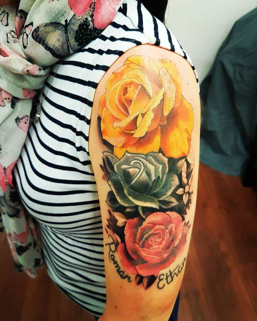 A vibrant rose sleeve tattoo featuring yellow, green, and red roses with the names "Roman" and "Ethan" beneath