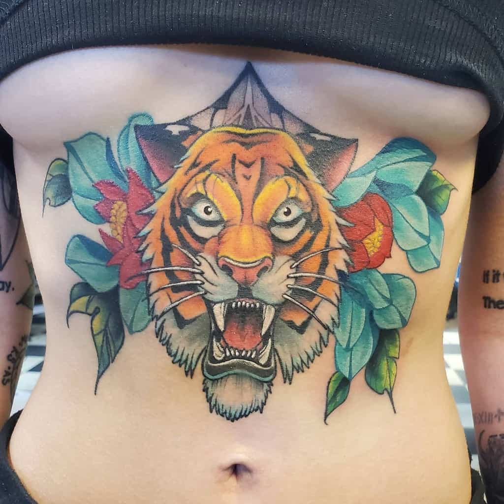A colorful tattoo of a roaring tiger with blue leaves and red flowers