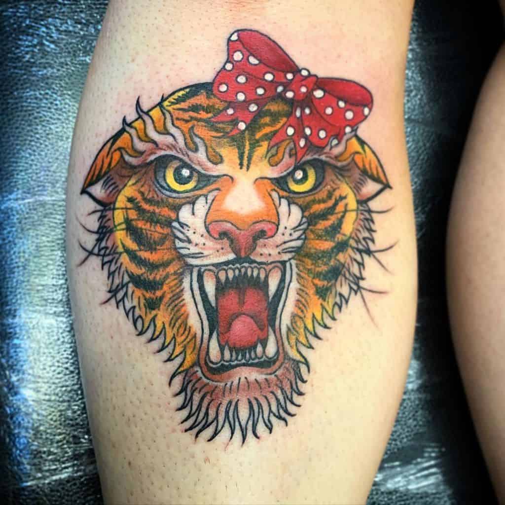 Tattoo of a snarling tiger's head with a red polka dot bow on its ear