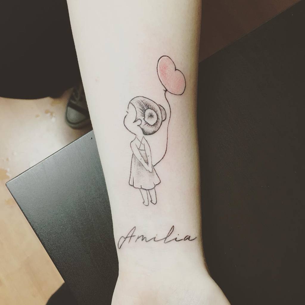 Delicate black ink tattoo of a little girl holding a pink heart-shaped balloon, with the name 'Amilia' written in cursive below