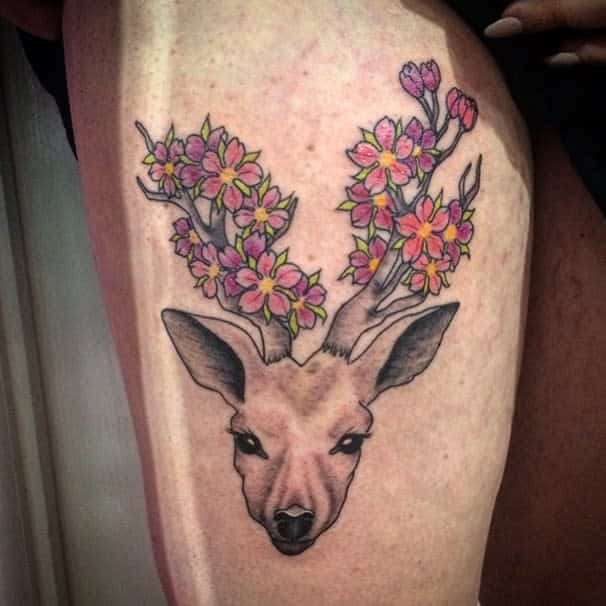 Elegant tattoo of a deer with antlers made of blooming pink and yellow cherry blossoms, blending realism and nature-inspired artistry