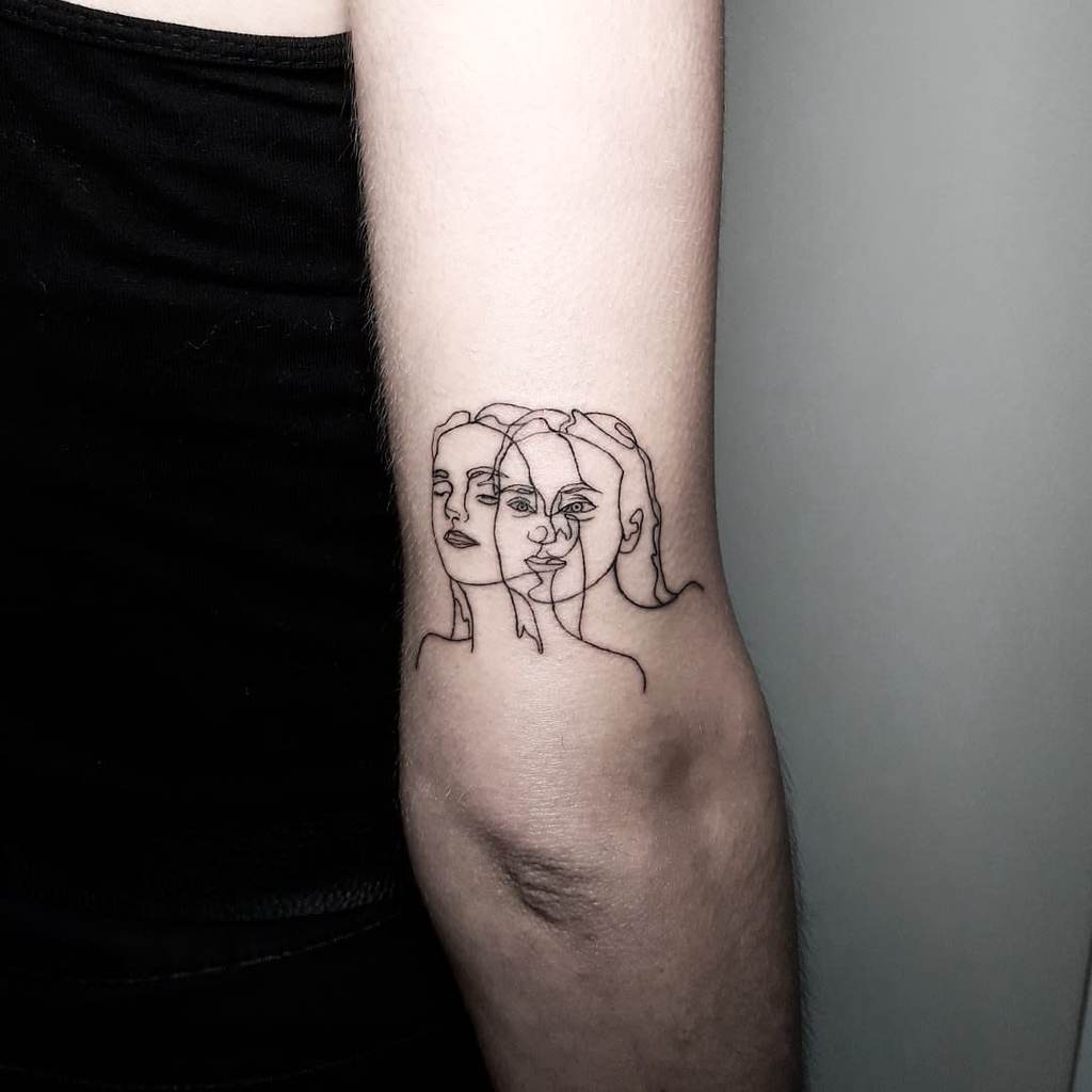 Minimalist tattoo of three overlapping, abstract female faces, with intricate black linework