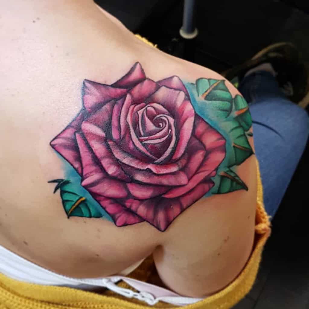 A vibrant red rose tattoo graces the shoulder, with lush green leaves elegantly trailing across a person's upper back