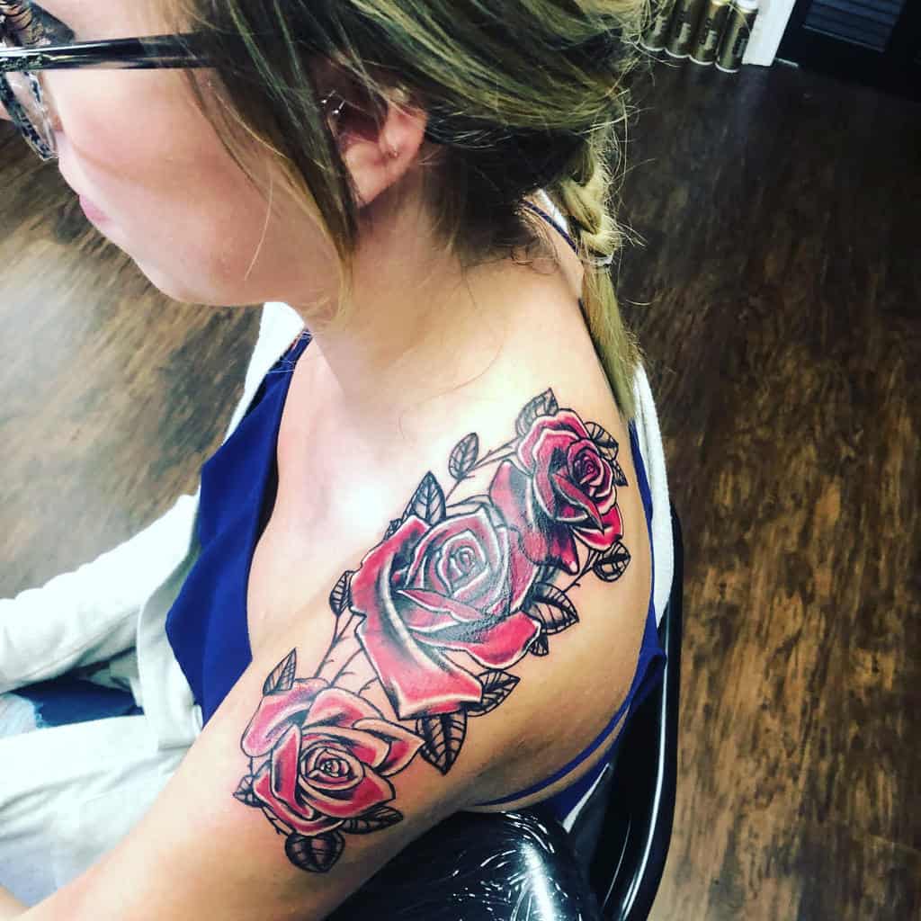 A feminine rose tattoo on the shoulder, featuring three vibrant red roses with detailed shading and black outlines