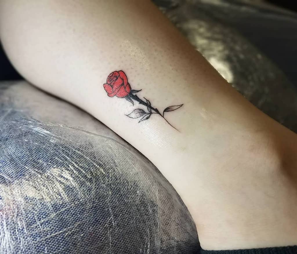 Ankle tattoo of a red rose with a green stem and leaves