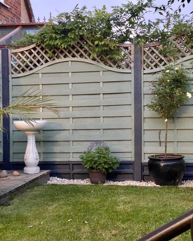 green wood fence with black base black pot plant white stone water feature